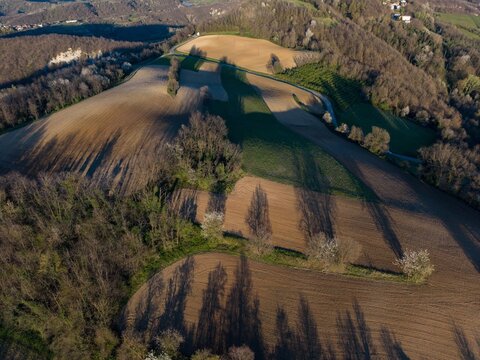 Aerial view of the Tortona Hills with cultivated fields, dense forests, and long shadows during late afternoon Tortona, Piedmont, Italy.