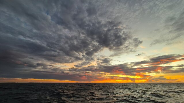 Stunning ocean sunset with dramatic clouds and vibrant orange hues reflecting on the water, capturing serene natural beauty.