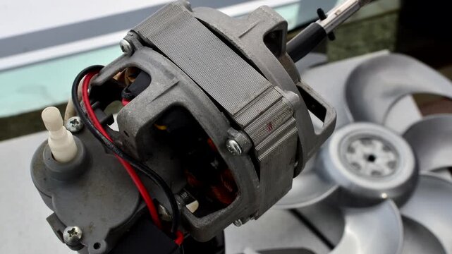 Close-up of an open fan motor, showcasing intricate wires and copper components in an industrial composition.