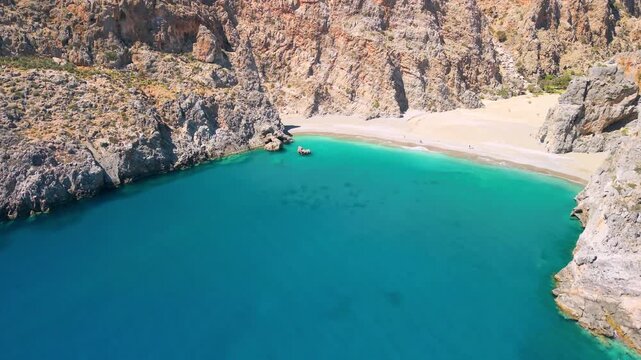 Aerial view of Agiofarango beach in Crete, Greece. Drone close up flight between sea rocks to empty beach and massive orange cliff. Scenic Mediterranean coastal landscape with turquoise water, 4k.