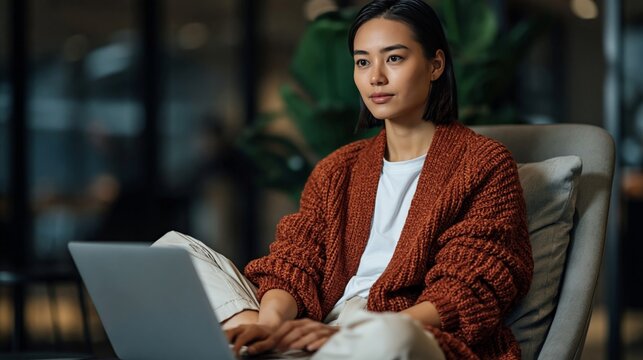 Asian woman working on laptop in modern office with plants. Remote work, digital productivity, and professional lifestyle concept.