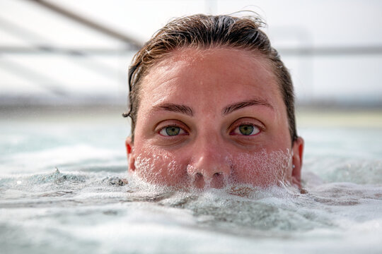 A beautiful lesbian woman in her thirties, face only somewhat submerged in a hot tub spa with bubbles on her face.  She has green eyes.
