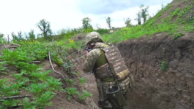 Infantry soldiers moving carefully along a trench, aiming and firing machine guns during active combat. Concept of frontline warfare, military tactics, and defensive movement in battle conditions