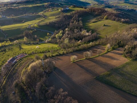 Aerial view of the Tortona Hills with rolling green slopes, cultivated fields, and winding roads under soft evening light in Tortona, Piedmont, Italy.
