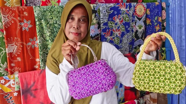 Proud senior asian artisan showing handmade beaded bags
