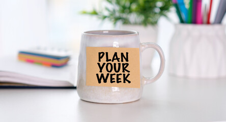 White ceramic mug sits on clean desk surface. Yellow label reads PLAN YOUR WEEK in bold black letters. © Pawel