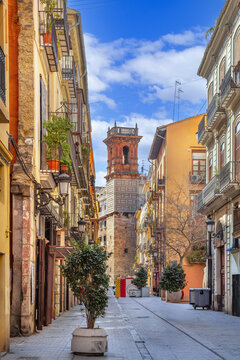 View of a street in Valencia, Spain, with a historic tower at the end. Old town urban landscape under sunny blue sky, no people