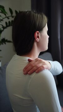 Tired unhappy young woman massaging hurt stiff neck sitting alone on couch at home, fatigued sad female rubbing tensed muscles to relieve joint shoulder pain, fibromyalgia concept	