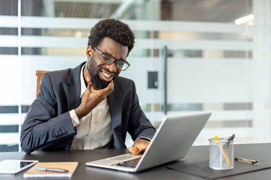Man in an office experiencing an uncomfortable toothache or gum pain while trying to focus on his laptop during a workday, representing health issues impacting professional productivity