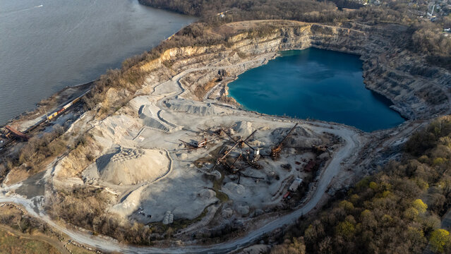 Aerial view of the Tomkins Cove quarry featuring a deep blue lake, industrial machinery, and gravel piles along the Hudson River in Stony Point, New York, United States.
