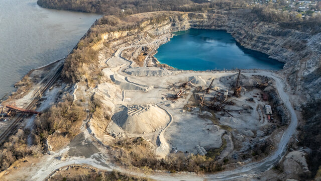 Aerial view of the Tomkins Cove quarry featuring a deep blue pool, industrial machinery, and gravel piles along the Hudson River in Stony Point, New York, United States.