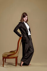 Naklejka premium Confident teenage girl in suit posing with chair in studio, full length portrait