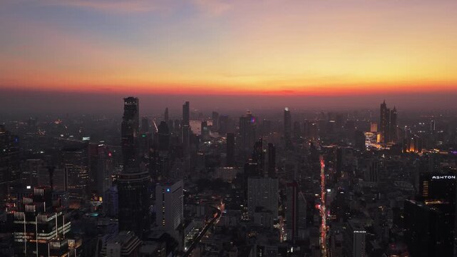 Aerial view of Bangkok skyline with its modern skyscrapers at dusk. City lights turn on while beautiful orange sunset colors the horizon