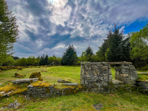 Stone ruins with partial doorway in grassy clearing at Cavan Burren Park, surrounded by woodland and dramatic cloud formations, County Cavan, Ireland