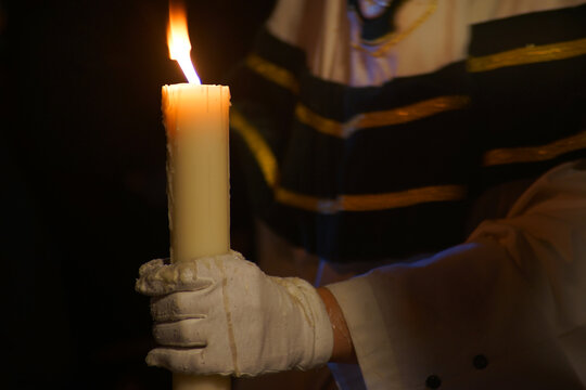 Person in white gloves holding a lit candle in the dark