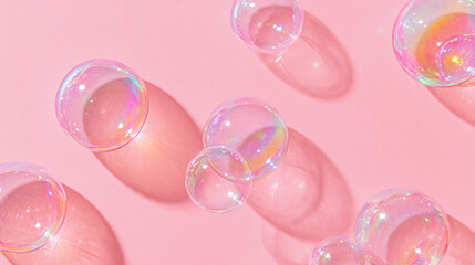 Fototapeta premium Transparent soap bubbles of various sizes floating against a soft pink background, casting delicate shadows and reflecting light in a playful, colorful display