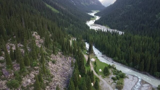 High angle view of traditional white yurts by winding river in deep mountain gorge, nomadic lifestyle concept, Tian Shan mountains, Kyrgyzstan, Karakol. High quality 4k footage
