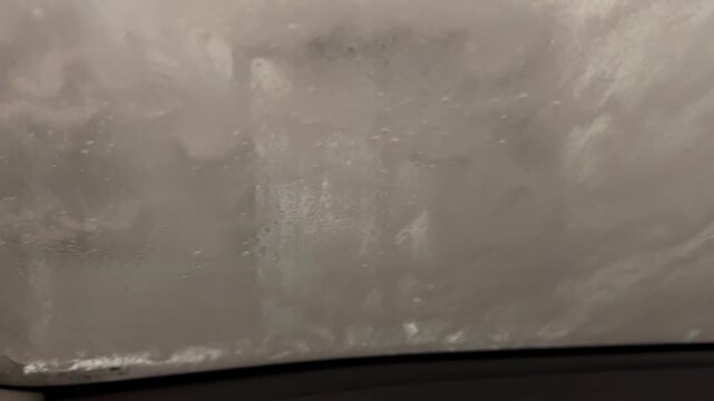 Close-up of foam and water flowing over car window in car wash, abstract liquid motion and transformation, cleaning concept with fresh texture and dynamic surface movement