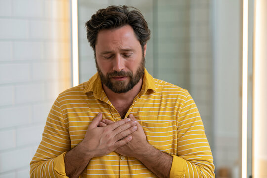 Man doing breathwork exercise during a moment of anxiety, hands on chest, eyes closed, standing in a bright bathroom mirror, self-regulation concept