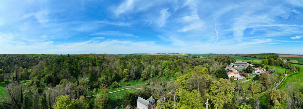 Aerial view of Roche Abbey ruins nestled within lush green woodlands and rolling hills under a bright blue sky with wispy clouds in Maltby, England, United Kingdom.