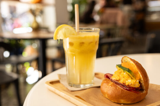 breakfast sandwich with brioche, egg, cheese, bacon, avocado, served with fresh squeezed citrus juice in a clear glass cup in a chic cafe
