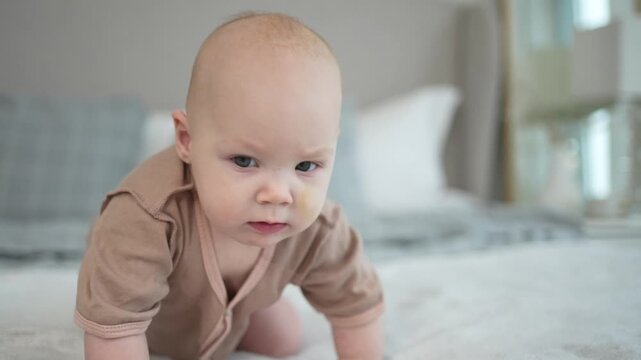 Happy baby. Cute little newborn girl with smiling face sitting on bed in bedroom. Infant baby resting playing crawling on blanket at home. Motherhood happy child childcare concept