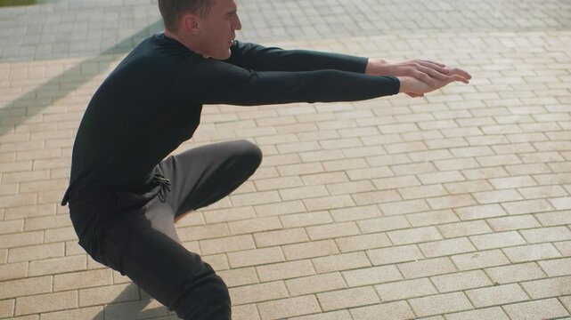 white man performing controlled squat in plaza arms extended steady descent sunlit paving focused trainer demonstrating bodyweight technique athlete testing balance core stability slow deliberate