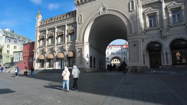 Moscow. Russia, 11.03.2026 People walking near historic building with double archway on sunny day. Urban street scene with pedestrians in city center. Architectural landmark travel concept.