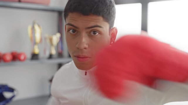 Man throwing a jab with red boxing gloves in a training studio with trophies on shelf; determination.