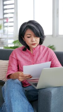 Older woman working on laptop reading document that made her frustrated, financial troubles, health concerns, bank debt notification, unexpected bills, feel distressed