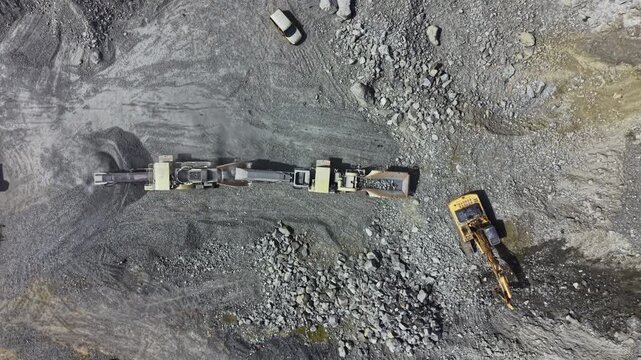 Large machines are extracting granite from a quarry site as workers oversee operations and transport materials nearby