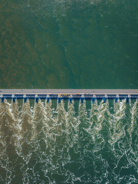 Aerial view of the Eastern Scheldt Storm Surge Barrier with water rushing through open sluice gates and cars driving along the top road in Vrouwenpolder, Zeeland, Netherlands.