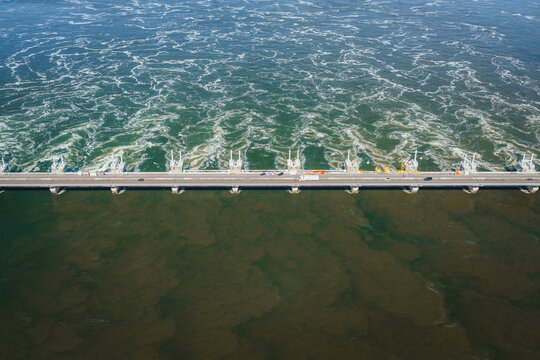 Aerial view of the Eastern Scheldt Storm Surge Barrier with turbulent water and cars driving across the bridge in Vrouwenpolder, Zeeland, Netherlands.