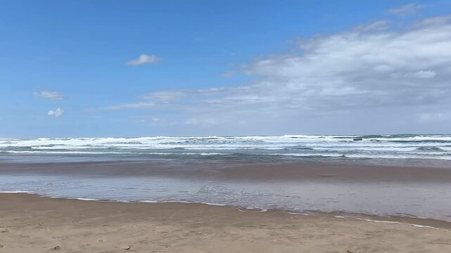 Cinematic footage of restless ocean waves rolling and crashing onto a sandy beach under bright sunlight.	