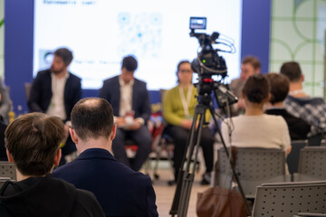 Fototapeta na wymiar Business panel recorded during seminar, audience watches while camera captures speakers, professional conference atmosphere.