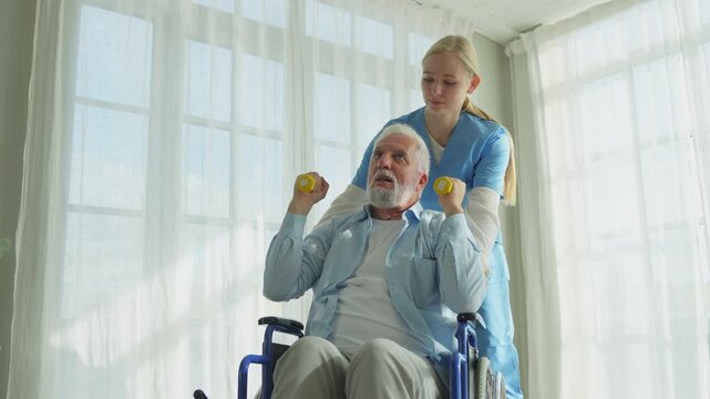 Support rehabilitation healthcare. Nurse helps old man patient in wheelchair picking up dumbbells. Paralyzed man in chair for people with disability doing sports exercise with nurse. Medical caregiver
