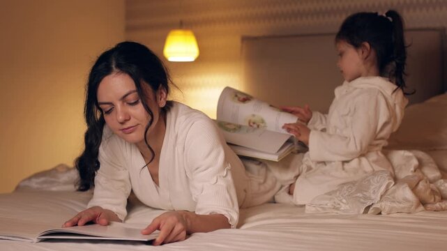 Happy mother and her cute little daughter reading bedtime stories in a cozy bedroom. Family enjoying a relaxing evening together at home
