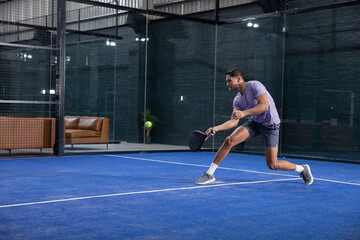Obraz premium African American male lunging and striking neon ball with black paddle on blue court, copy space