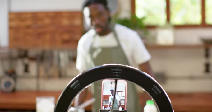 Ring light phone recording, African male in green apron stepping to counter, using mixing bowl