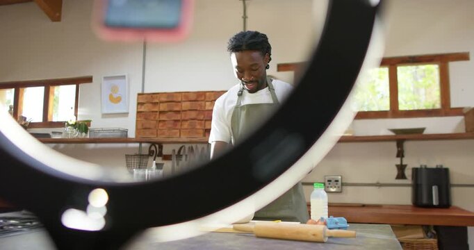Man in green apron whisking batter in kitchen for demo with ring light shifting, revealing flour