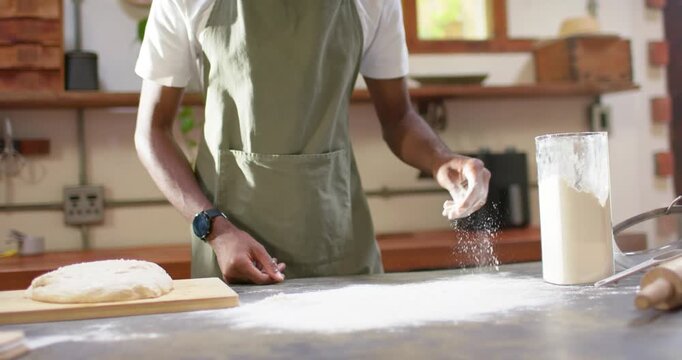African American man prepping dough on board, sprinkling and scooping flour from clear container