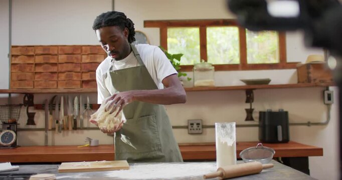Adult African baker pressing, stretching sticky dough on counter, forming loaf, camera rig visible