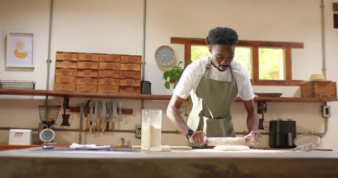 After placing dough African man in apron using rolling pin flattening dough for baking in bakery