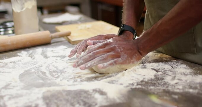 Male cook in apron from loose dough folding pressing at floured-counter near rolling pin for baking