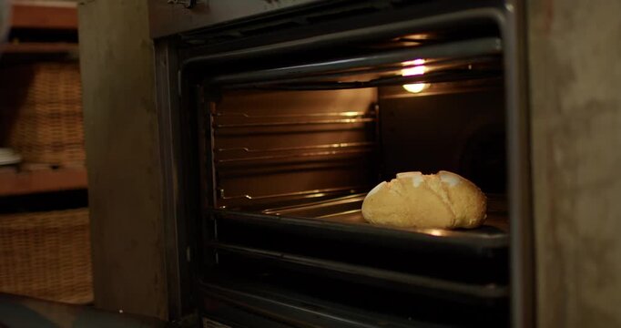 Person is opening oven door in kitchen, gripping tray and pulling round loaf out to cool