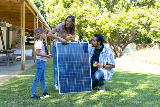 Family with daughter checking upright solar panel on yard near patio holding juice glasses