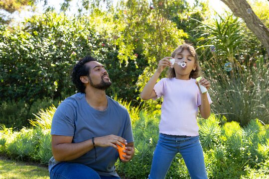 African American father-daughter blowing bubbles in sunny yard with orange bottle and wand