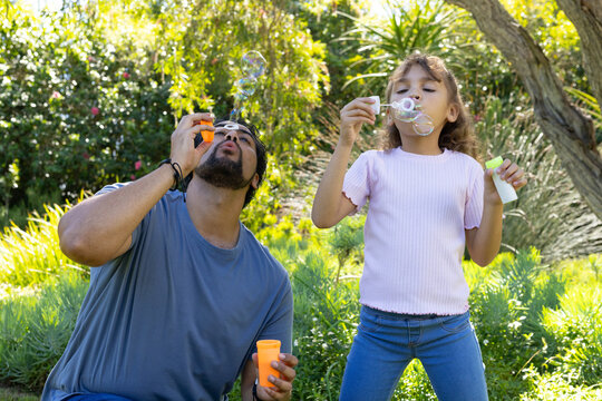 African American father and youth girl blowing bubbles in garden with orange, white bottles, wands