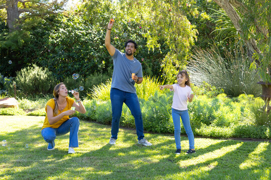 Family of two adults and child playing with bubbles using wands and bottles in backyard garden