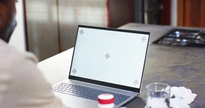 Man sitting at kitchen counter watching blank laptop screen with targets, adjusting for webcam